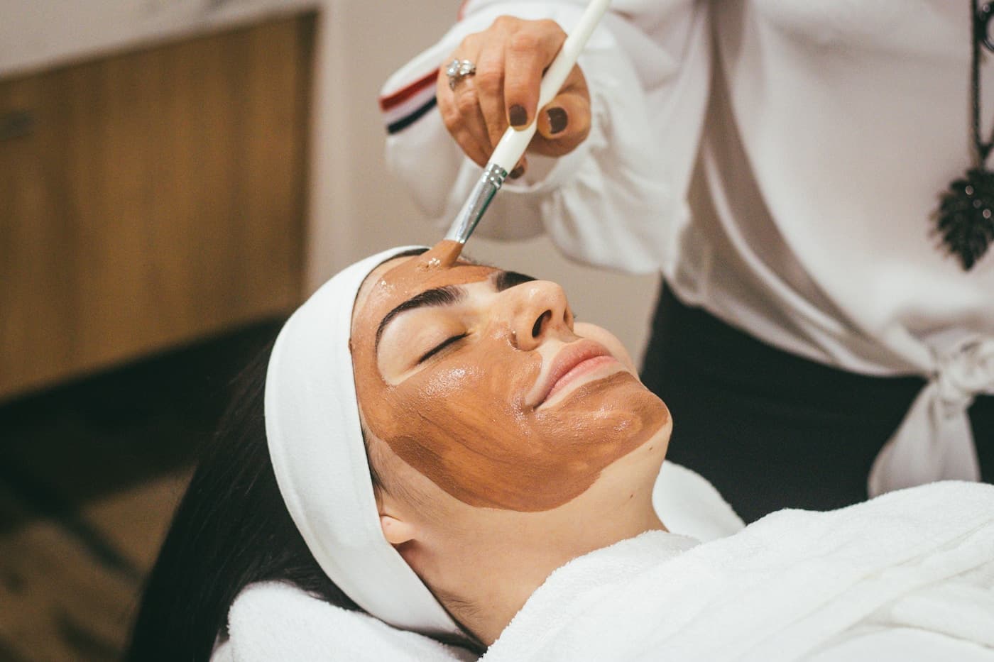 Application d'un masque de soin sur le visage d'une cliente détendue